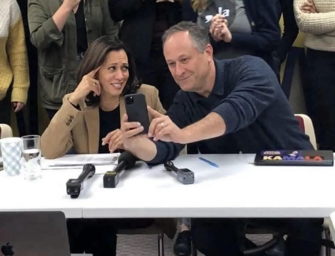 Doug Emhoff showing Kamala Harris a cell phone whilst she rolls her eyes.